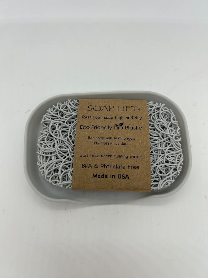 May include: White soap dish made of eco-friendly bio plastic. The dish is shaped like a web and has a label that reads "SOAP LIFT&reg; Rest your soap high and dry Eco Friendly bio Plastic Bar soap will last longer. No messy residue. Just rinse under running water! BPA & Phthalate Free Made in USA"