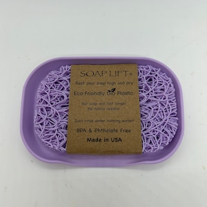 May include: Purple soap dish made of eco-friendly bio plastic. The dish features a raised, web-like design to keep soap elevated and dry. The text on the label reads "SOAP LIFT&reg; Rest your soap high and dry. Eco Friendly bio Plastic Bar soap will last longer. No messy residue. Just rinse under running water! BPA & Phthalate Free Made in USA"