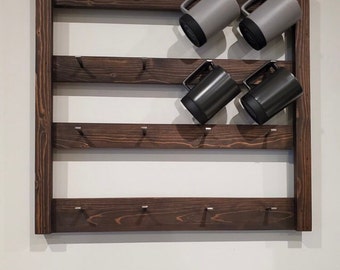 May include: A dark brown wooden mug rack with four shelves and multiple hooks for hanging mugs. The rack is mounted on a white wall. There are four mugs hanging on the rack, two gray and two black.