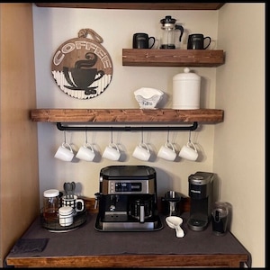 May include: A rustic coffee station with wooden shelves, a black pipe rail with hanging mugs, a coffee maker, a Keurig coffee machine, and a sign that says "Coffee".