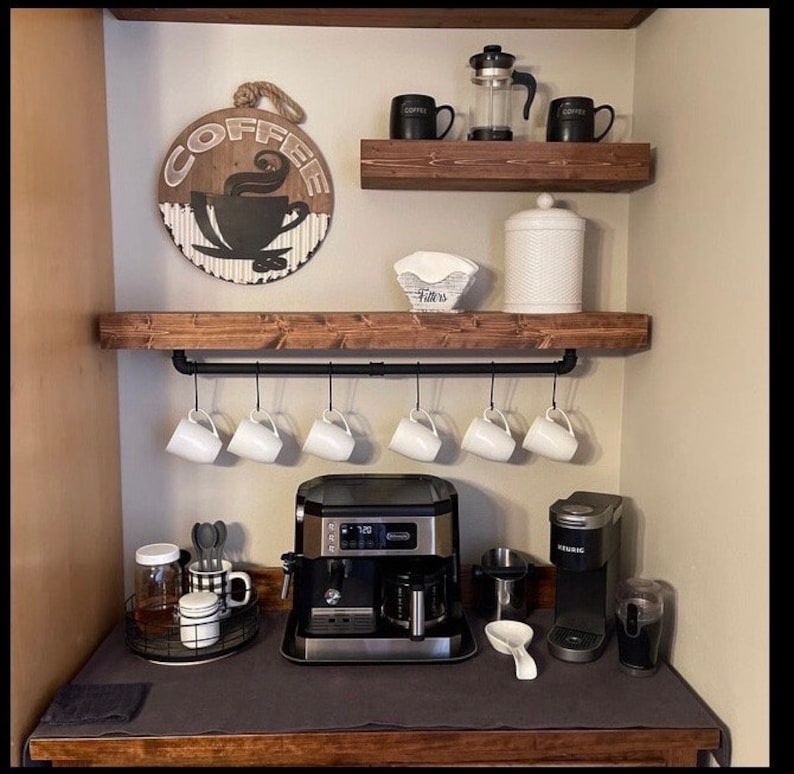 May include: A rustic coffee station with wooden shelves, a black pipe rail with hanging mugs, a coffee maker, a Keurig coffee machine, and a sign that says "Coffee".