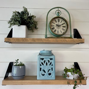 May include: Two wooden shelves with black metal brackets, decorated with potted plants, a blue lantern, and a vintage clock with a green metal frame.