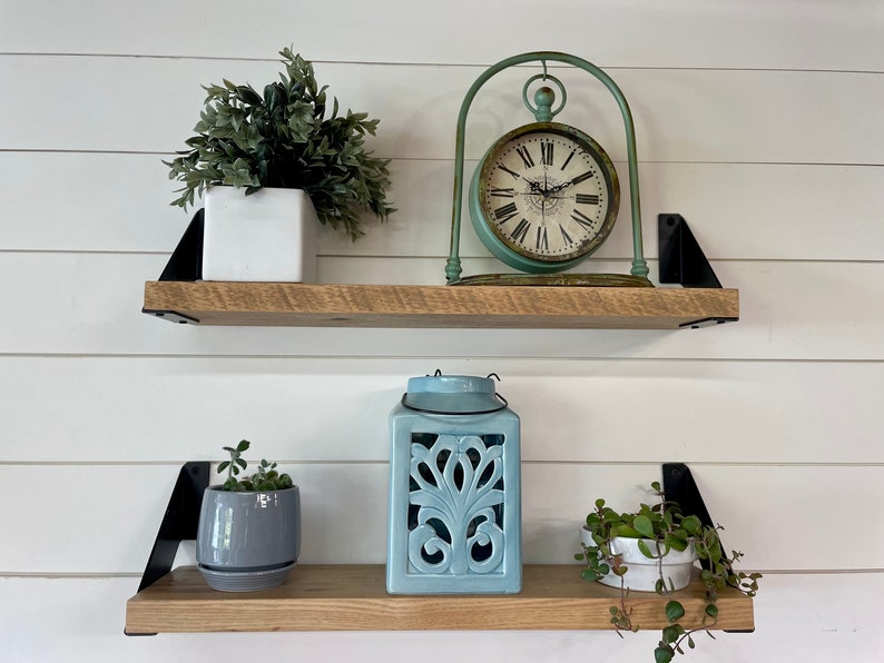 May include: Two wooden shelves with black metal brackets, decorated with potted plants, a blue lantern, and a vintage clock with a green metal frame.