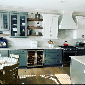 May include: A modern kitchen with white cabinets, gray subway tile backsplash, and green cabinets. The kitchen features a stainless steel wine cooler, a farmhouse sink, and a white range hood.