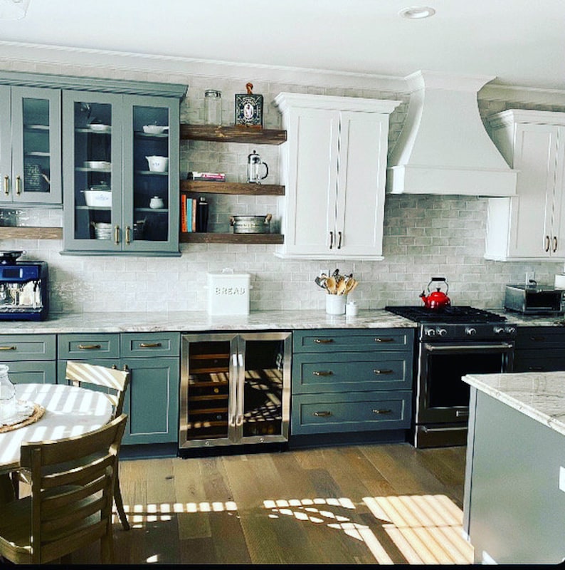 May include: A modern kitchen with white cabinets, gray subway tile backsplash, and green cabinets. The kitchen features a stainless steel wine cooler, a farmhouse sink, and a white range hood.
