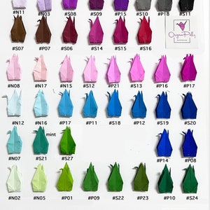 May include: A collection of origami cranes in various colours, including white, ivory, cream, orange, pink, purple, blue, green, red, gold, and silver. The cranes are arranged in rows on a white background. Each crane is labelled with a number.