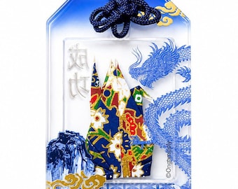 May include: A rectangular clear acrylic omamori charm featuring a blue dragon illustration, a floral patterned origami crane, and gold cloud accents. The charm includes the text "SUCCESS" and Japanese characters, topped with a dark blue cord.