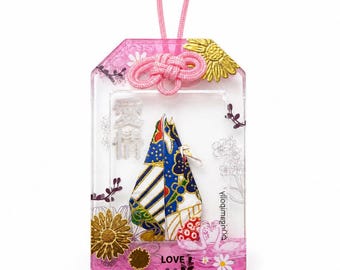 May include: A rectangular clear resin charm featuring a pink cord, a gold sunflower, and a central origami-style paper insert with blue, white, and gold patterns. The charm includes the Japanese characters for love, the word LOVE, and two white swan illustrations.