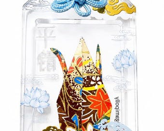 May include: A rectangular clear acrylic omamori charm featuring a folded paper crane with a multi-colored floral pattern. The charm includes gold cloud accents, blue lotus illustrations, and the text "INNER PEACE" printed in blue at the bottom.
