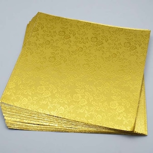 May include: A stack of gold cardstock paper with a floral pattern. The paper is embossed with a subtle texture.