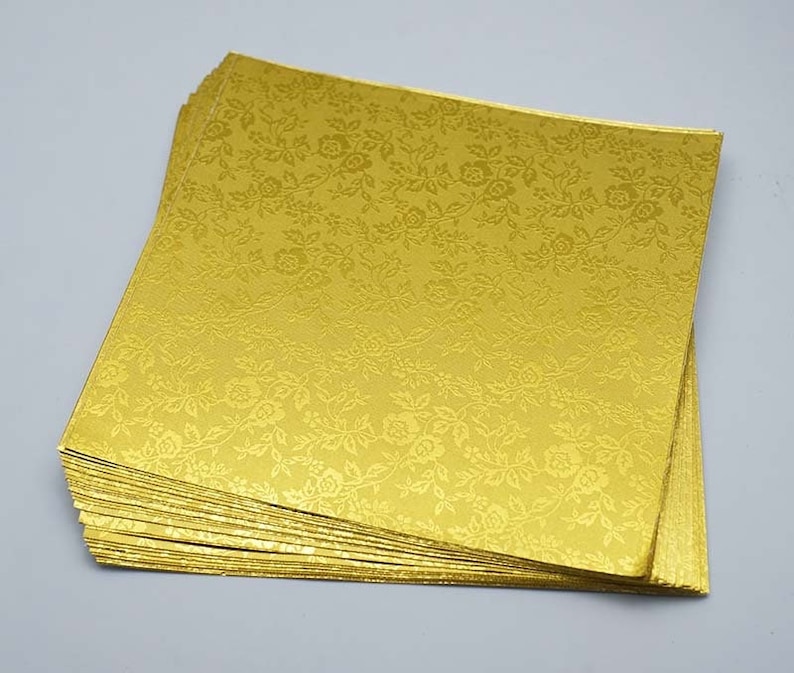 May include: A stack of gold cardstock paper with a floral pattern. The paper is embossed with a subtle texture.