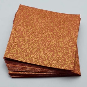 May include: A stack of orange cardstock paper with a gold embossed paisley pattern.