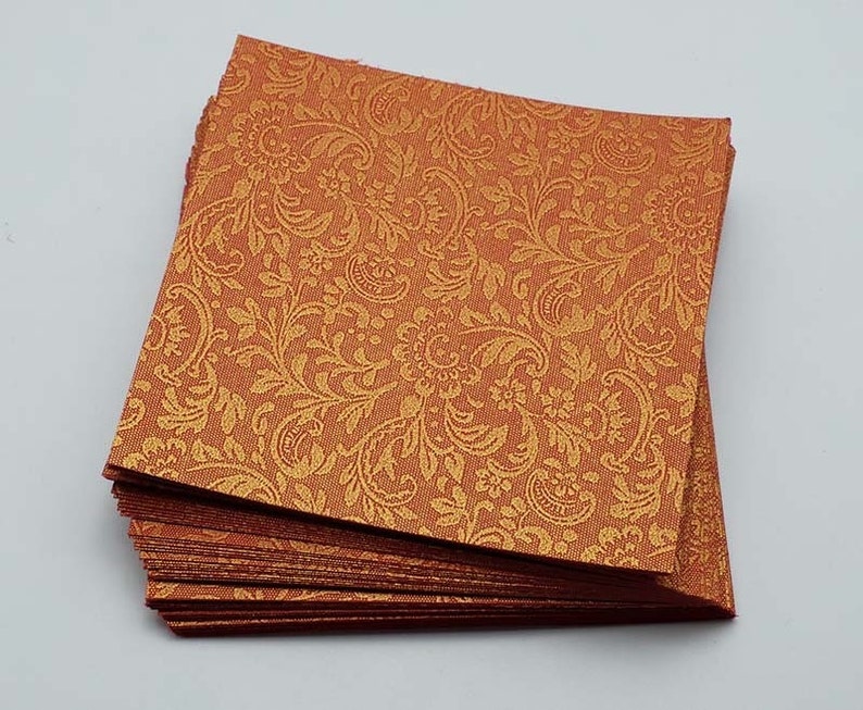 May include: A stack of orange cardstock paper with a gold embossed paisley pattern.