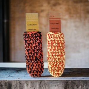 May include: Two crocheted pot holders, one black and orange, the other yellow and orange. The pot holders are labeled "Cast Iron Skillet Handle Cover".