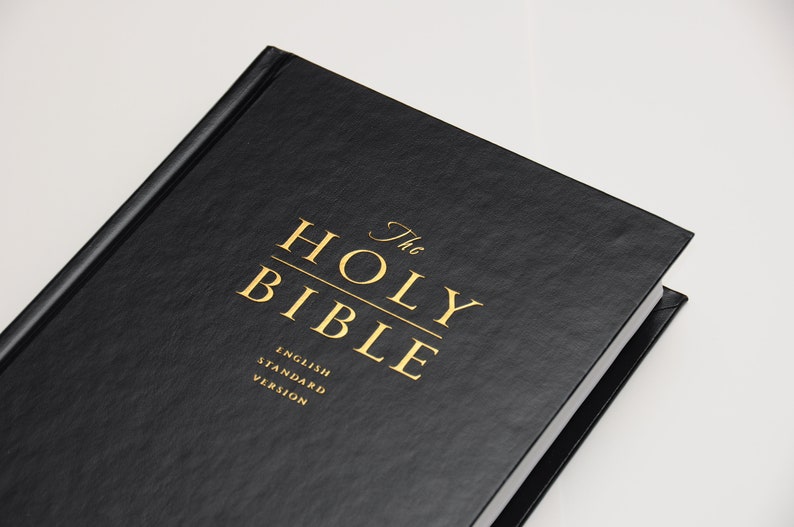 May include: A black hardcover book titled "The Holy Bible" with gold lettering. The text "English Standard Version" is also visible. The book is set against a white background.
