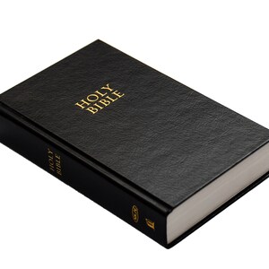 May include: A black hardcover book with the words "HOLY BIBLE" in gold lettering on the cover. The book has a textured surface and white-edged pages. The spine also has the words "HOLY BIBLE" in gold.