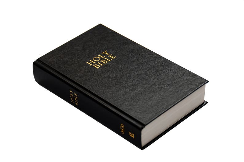 May include: A black hardcover book with the words "HOLY BIBLE" in gold lettering on the cover. The book has a textured surface and white-edged pages. The spine also has the words "HOLY BIBLE" in gold.