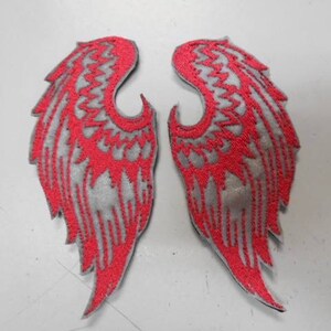 May include: Two red and gray embroidered angel wings patches. The wings are detailed with a zig-zag pattern and have a gray background with red stitching.