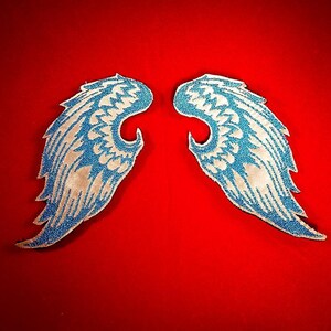 May include: Two blue and white angel wings with a sparkly finish. The wings are on a red background.