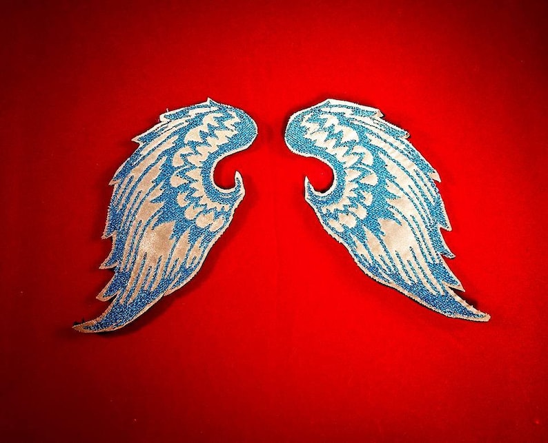 May include: Two blue and white angel wings with a sparkly finish. The wings are on a red background.