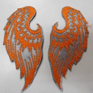 May include: A pair of iron-on patches featuring a silver and orange embroidered design of angel wings.