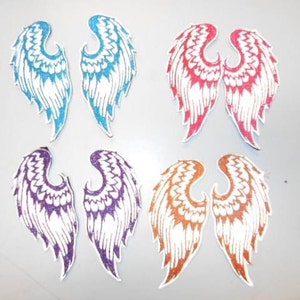 May include: Set of six iron-on patches featuring angel wings in various colors, including blue, purple, red, and orange. The wings are white with glitter accents.