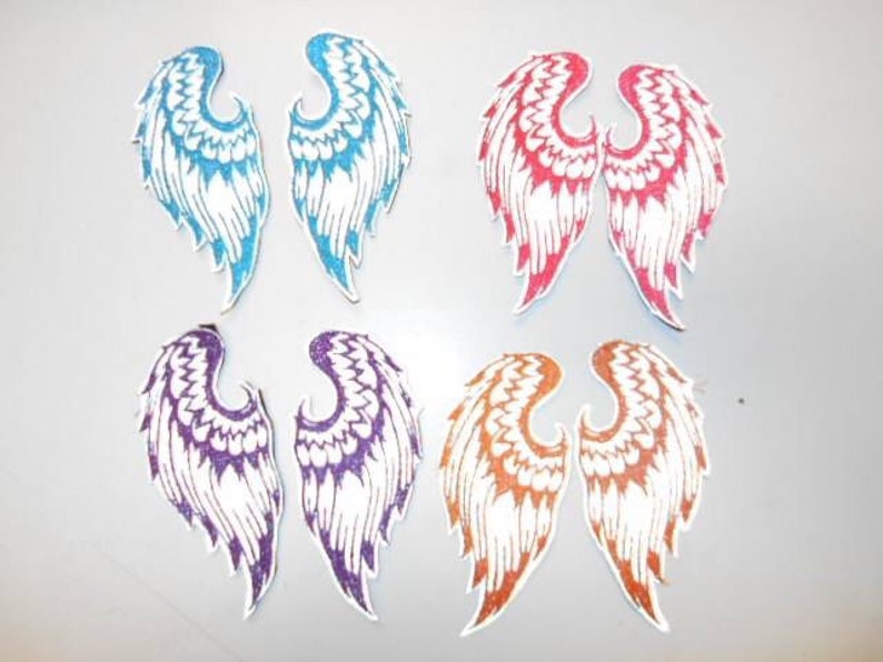 May include: Set of six iron-on patches featuring angel wings in various colors, including blue, purple, red, and orange. The wings are white with glitter accents.