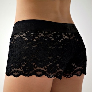 May include: Black lace boxer shorts with a floral pattern. The waistband is black with the word "BOXERS" printed on it. The shorts are made of a delicate, see-through lace material.