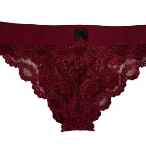 May include: Burgundy lace underwear with a black bow detail. The underwear has a wide waistband and a delicate lace pattern.