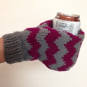 May include: A gray and pink striped knitted mitten with a can of soda inside. The can has a nutrition facts label.