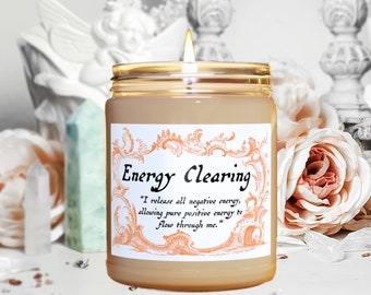May include: A beige candle in a glass jar with a gold lid. The label on the jar is white with an orange floral design and the text "Energy Clearing" and "I release all negative energy, allowing pure positive energy to flow through me."