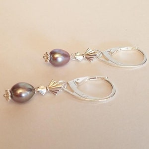 May include: A pair of silver hoop earrings with a single dark gray pearl dangling from each hoop.