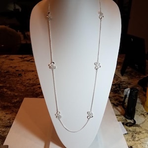 May include: A silver necklace with five flower-shaped pendants. Each pendant has a cluster of small, clear crystals.