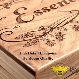 May include: A wooden box with a detailed engraving of the word "Essence" and floral designs. The box is made of light wood and has a natural finish. The text "High Detail Engraving Heirloom Quality" is printed on the box. A bee logo with the text "Designer Bee of New England Let's Make it Personal" is printed on the bottom right corner of the box.