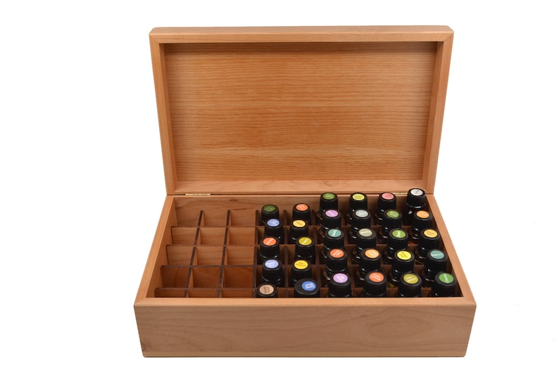 May include: A wooden box with a hinged lid, containing a grid of small glass bottles with colorful labels. The box is made of light wood and has a natural finish.