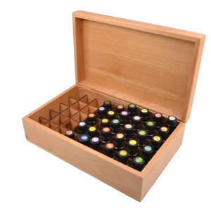 May include: A wooden box with a hinged lid, open to reveal a compartmentalized interior filled with small glass bottles. The bottles have colorful caps and are arranged in rows.