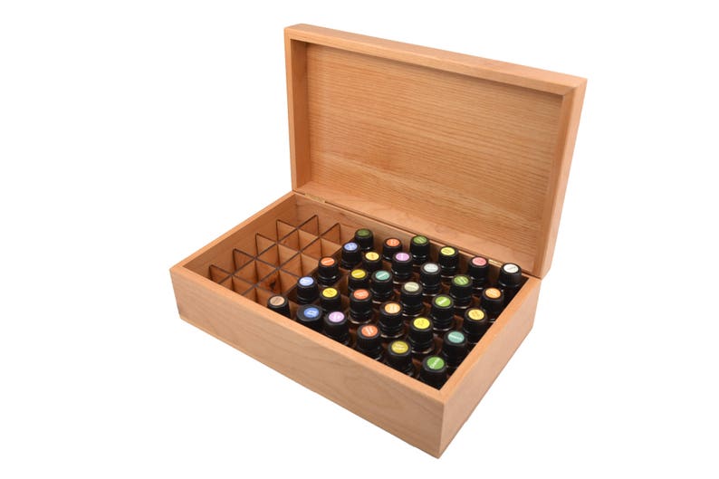 May include: A wooden box with a hinged lid, open to reveal a compartmentalized interior filled with small glass bottles. The bottles have colorful caps and are arranged in rows.