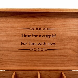 Op de afbeelding: Een houten doos met een scharnierend deksel. Het deksel is open en de binnenkant is gegraveerd met de tekst "Time for a cuppie! For Tara with love."