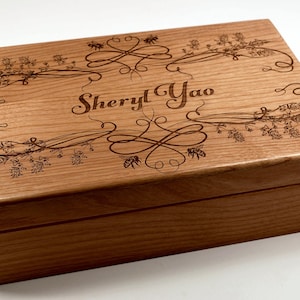 May include: A wooden box with an engraved design of flowers and bees. The box is personalized with the name "Sheryl Yao".