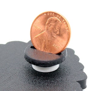 May include: A black plastic coin holder with a white base. A copper-colored 2021 US penny is resting in the holder. The penny has the words "IN GOD WE TRUST" and "LIBERTY" on it.
