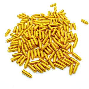 Könnte beinhalten: Ein großer Haufen goldfarbener Patronenhülsen auf weißem Hintergrund.