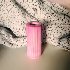 May include: A pink cylindrical candle holder with a ribbed texture. The holder is empty and has a white interior.