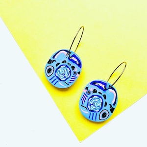 May include: A pair of blue and white hoop earrings with a colorful abstract design. The earrings are made of polymer clay and have a gold hoop.