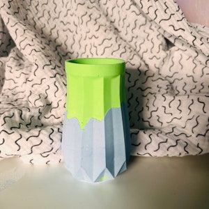 May include: A light blue and green ceramic vase with a geometric design. The vase has a wide base and a narrow neck.