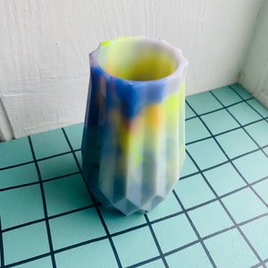 May include: A small, geometric, multi-colored vase with a white, yellow, and blue marbled design. The vase is made of ceramic and has a textured surface.