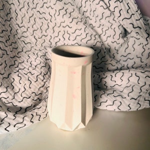 May include: White geometric ceramic planter with pink speckles. The planter has a wide base and a narrow opening.
