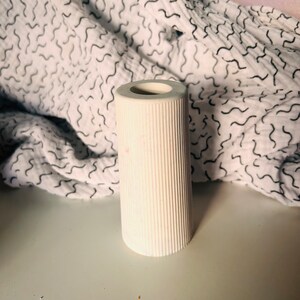 May include: White ceramic candle holder with a ribbed texture. The holder is cylindrical and has a smooth, rounded top.
