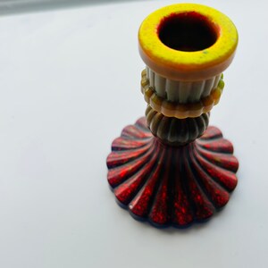 May include: A decorative candlestick with a red, glittery base and a brown, ridged body. The top rim is yellow. The candlestick has a unique, ornate design, suitable for home decor.