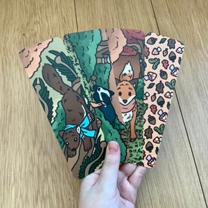 Puede incluir: Cuatro marcapáginas ilustrados con animales del bosque. Los marcapáginas están impresos en cartulina y presentan un zorro, un tejón, una ardilla y un patrón de hojas y bellotas.