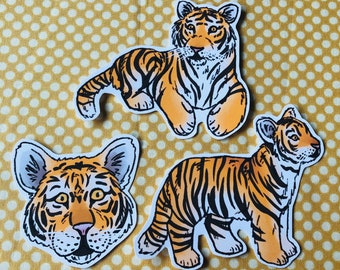 May include: Three tiger stickers with orange and black stripes. The stickers are on a yellow polka dot background.